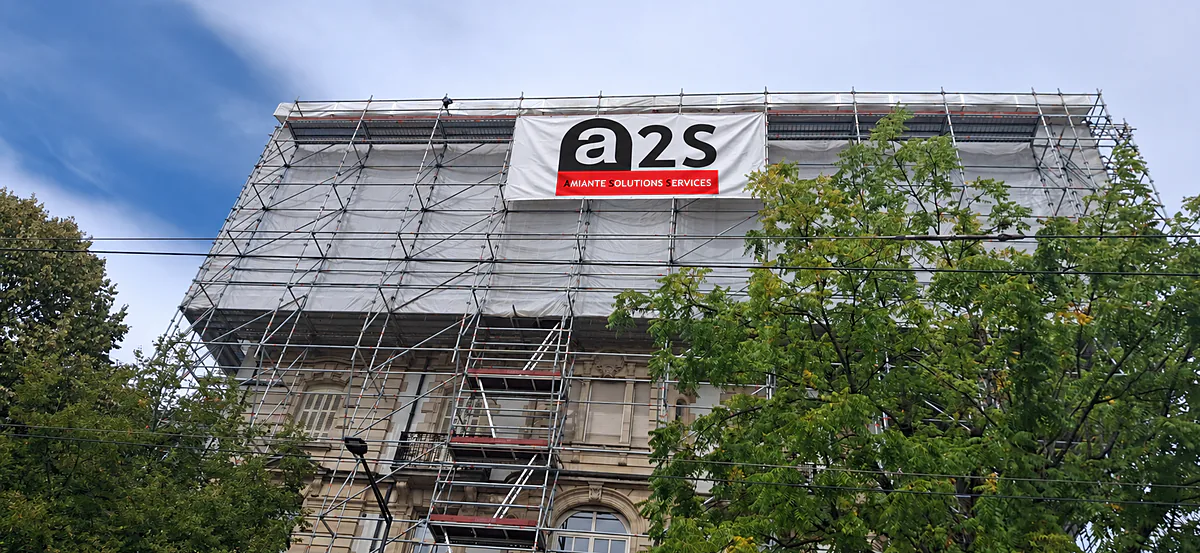 Façade d'immeuble sous échafaudage bâché, avec la bannière A2S - Amiante Solutions Services
