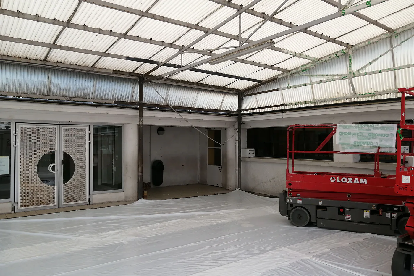 Préparation d'un chantier de déplombage : sol du hall protégé par un polyane, élévateur à ciseaux en place