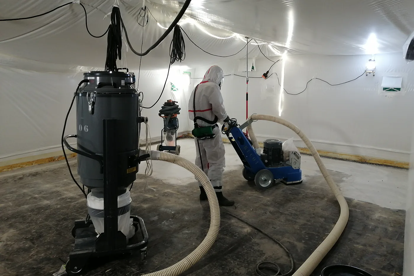 Ponçage d'un revêtement de sol en zone confinée par un opérateur en combinaison et masque respiratoire