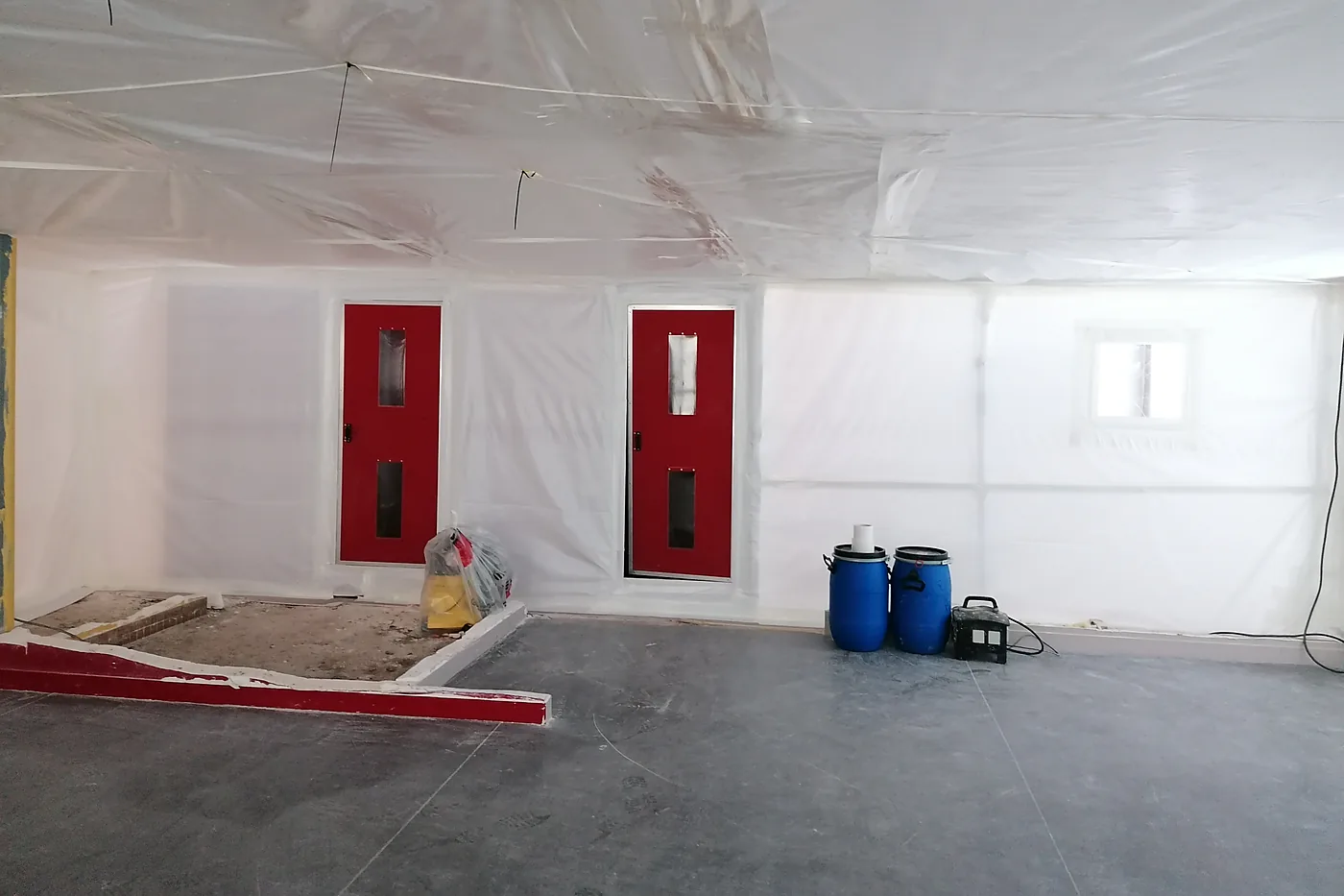 Zone de travaux confinée sous films plastiques, avec ses sas d'accès aux portes rouges